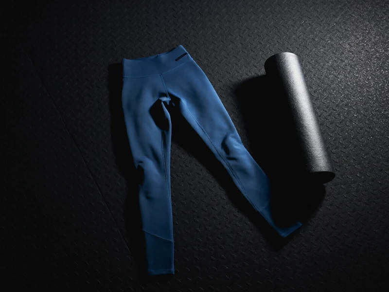 Marineblaue Kompressions-Leggings flach auf schwarzem Gummiboden neben einer Yogamatte, Illustration