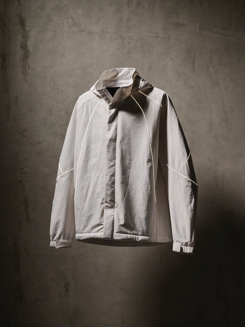 Naturweisse Windjacke mit reflektierenden Paspeln an einer rohen Betonwand, Illustration